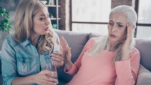 Jonge dame probeert oudere vrouw te helpen met medicijnen en water Jonge dame probeert oudere vrouw te helpen met medicijnen en water