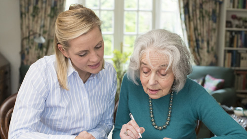Jonge vrouw helpt oudere dame met het invullen van gegevens Jonge vrouw helpt oudere dame met het invullen van gegevens